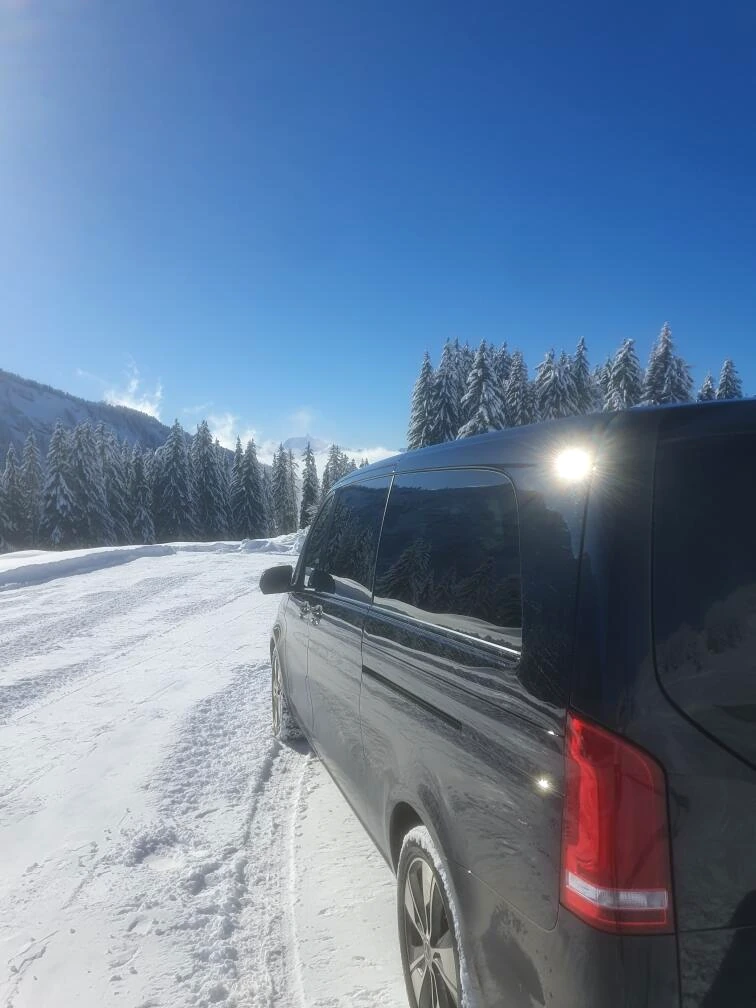 Leocleme Prestige Mercedes V-Class van on a snowy mountain road surrounded by Alpine forests.